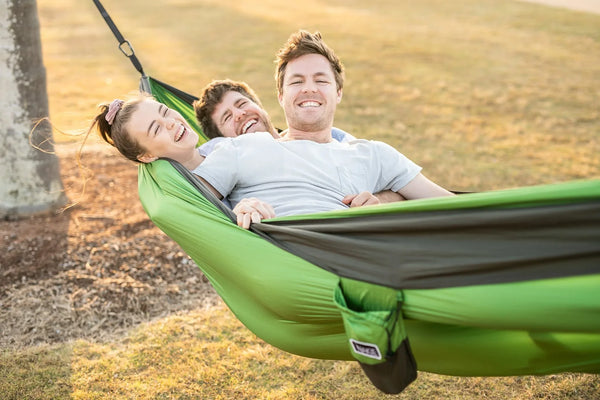 Green and grey double hammock with two people and a child relaxing in it outdoors