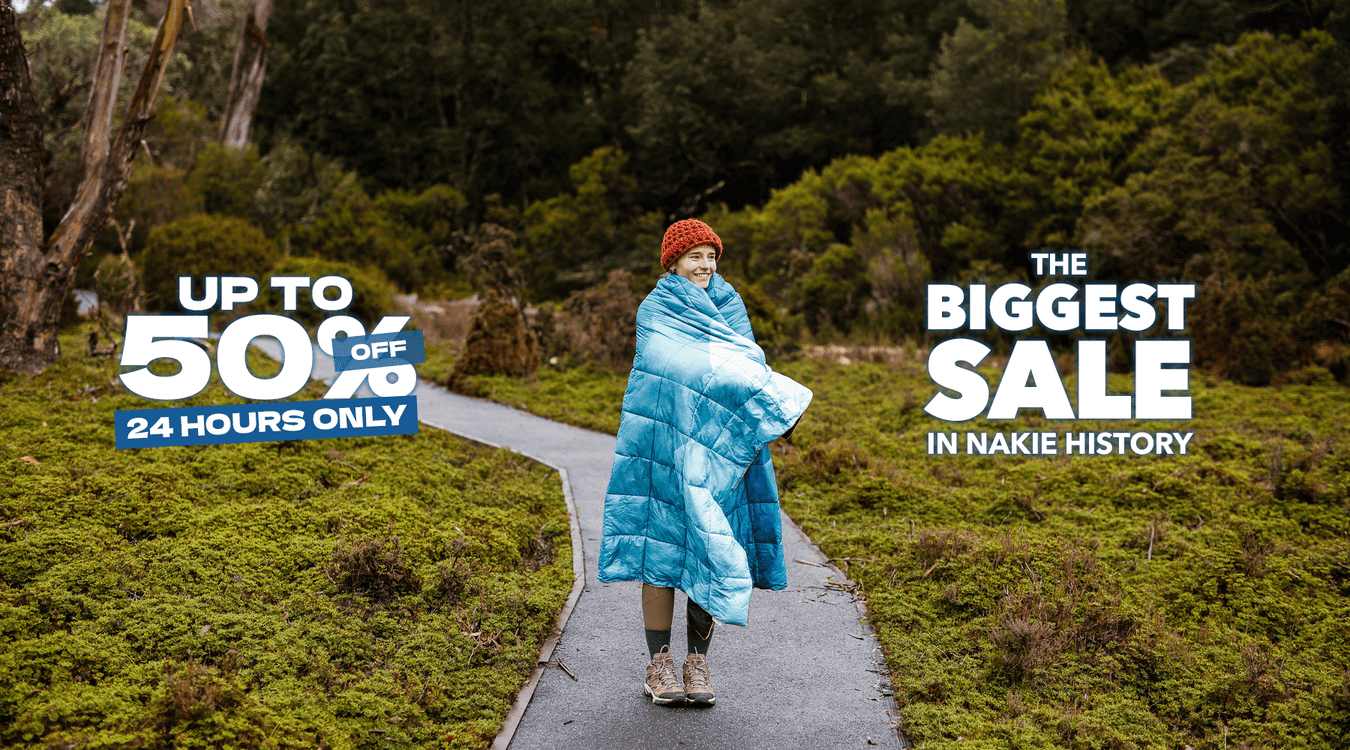 Two people wrapped in a blue puffy blanket sitting on a mountain edge