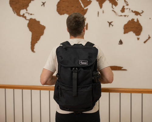Black recycled travel backpack with flap closure, side pockets, and branded label, worn on back view.
