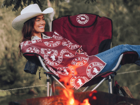 Burgundy recycled beach towel with white circular logo pattern, draped over camping chair by campfire