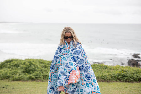 White, blue, and coral geometric patterned sustainable down puffy blanket draped around person at beach