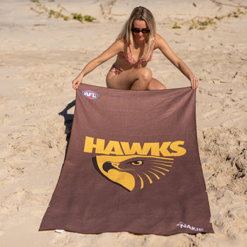 Brown beach towel with yellow Hawks logo and AFL branding, displayed on sand