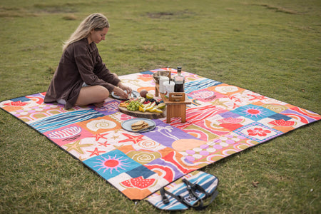 Retro Shores recycled picnic blanket with colorful beach-themed pattern in use on grass during outdoor picnic.