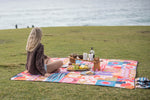 Colorful patterned picnic blanket with retro geometric design, spread on grass by ocean during seaside picnic setup. preview #6