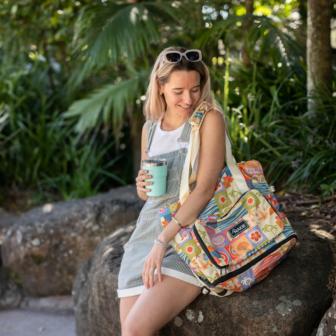 Retro Shores recycled tote bag with colorful beach-themed print, carried by woman in outdoor garden setting.