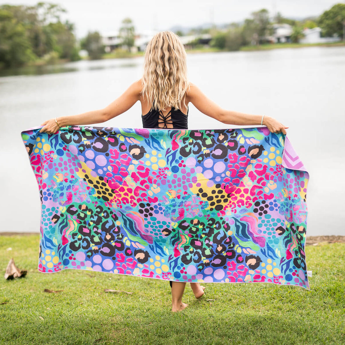 Recycled sand-free beach towel with multicoloured leopard and geometric print, displayed outdoors by water