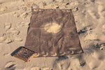 Brown recycled beach towel with celestial sun and moon design, laid flat on sand with matching pouch preview #12