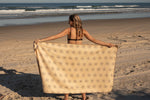 Cream beach towel with all-over star pattern, held open by woman in bikini on sandy beach with ocean waves behind preview #11