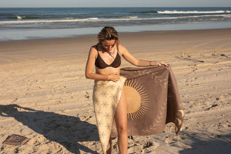 Recycled sand-free beach towel in taupe with sun and leaf print design, displayed on beach