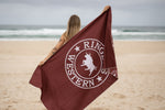 Burgundy beach towel with white circular logo featuring bull and Ringers Western text, held by person on sand. preview #8
