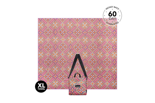 XL beach towel in pink and orange geometric pattern, displayed flat with black carry straps and storage pouch.