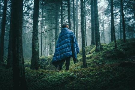 Man nestled amidst the tranquil woods, wrapped in a Nakie puffy blanket, enjoying warmth and comfort during an outdoor adventure in nature